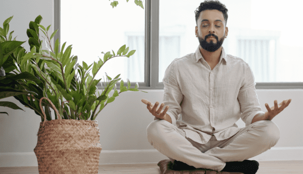 Your Baby’s Fine. Take Care of Yourself A man sitting down on the floor ontop of a pillow and meditating in a crosslegged position